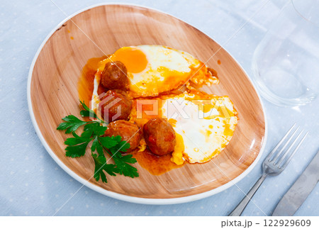 Plate of fried eggs and meatballs with sauce and greens 122929609