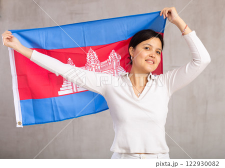 Reliant positive young woman holds big national flag of Cambodia with confident smile showing teeth 122930082
