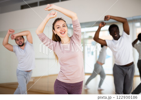 Young woman practicing vigorous dance movements with group 122930186