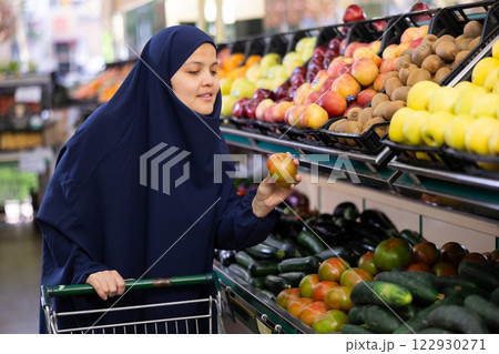 Woman in paranja shopping and choosing local tomatoes in hypermarket Woman in paranja shopping and choosing local tomatoes in hypermarket 122930271
