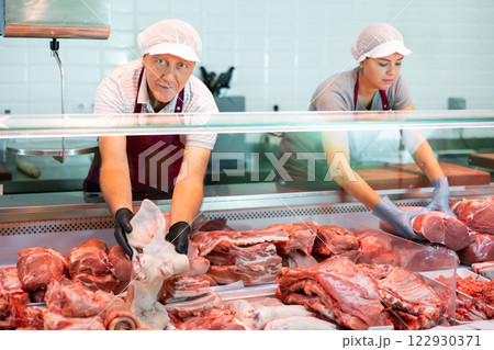 Elderly butcher shop owner arranging pork pieces in display case Elderly butcher shop owner arranging pork pieces in display case 122930371