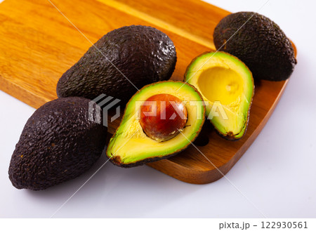 Whole and halved avocados on wooden cutting board on white 122930561