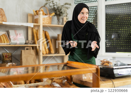 Saleswoman in a hijab collects pastries in a container Saleswoman in a hijab collects pastries in a container 122930666