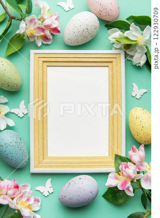 Easter eggs and flowers bordering a blank frame on a turquoise background 122930709