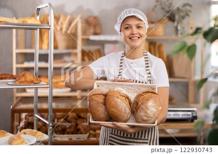 Middle-aged saleswoman displays sourdough bread in wicker basket 122930743