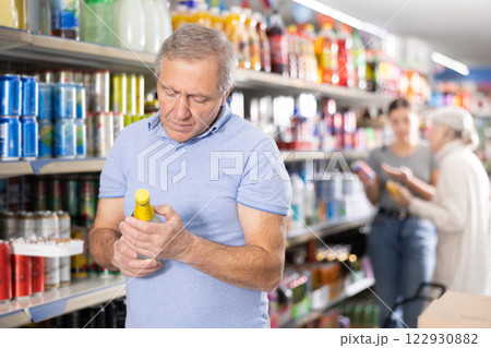 Aged man reading labels while choosing soft drink in supermarket Aged man reading labels while choosing soft drink in supermarket 122930882