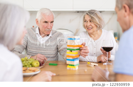 Group of four mature friends is playing board game with wooden blocks in kitchen 122930959
