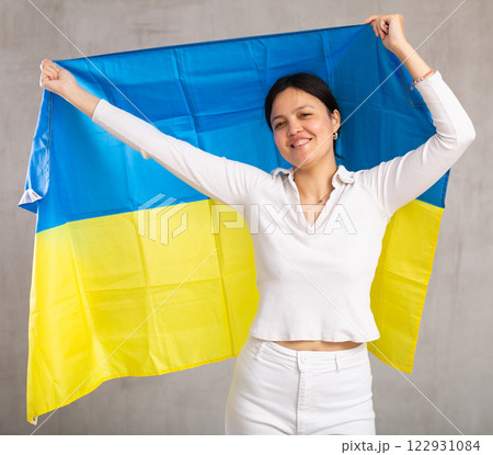 Middle-aged woman in casual clothes holds unfurled flag of Ukraine in hands raised above head 122931084