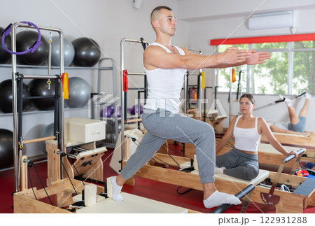 Sportive young guy training her arms and legs on reformer device 122931288