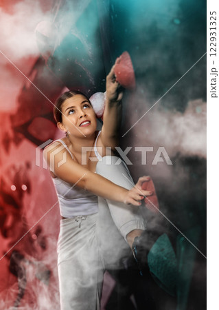 Young europian woman visitor to fitness club climbs wall for amateur sportsmen, neon light. 122931325
