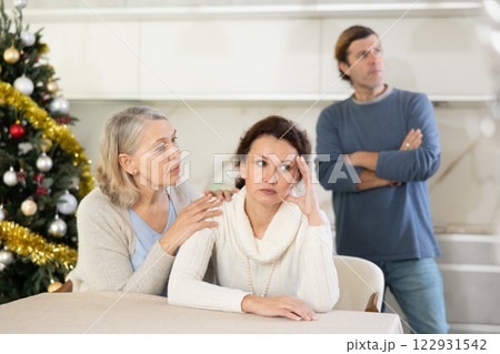 Senior woman sits near daughter and comforts during quarrel with husband on Christmas Eve Senior woman sits near daughter and comforts during quarrel with husband on Christmas Eve 122931542