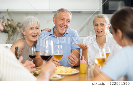 Cheerful elderly women and man gathering around kitchen table Cheerful elderly women and man gathering around kitchen table 122931590