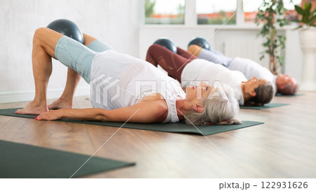 Lady does lightweight bridge pose - Setu Bandhasana and holds softball in lap. 122931626