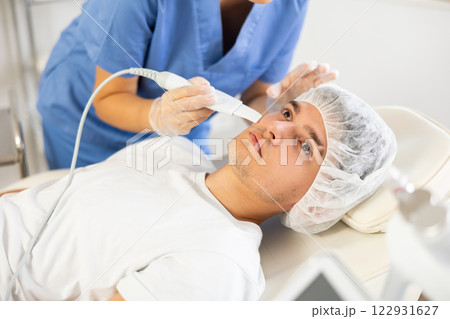 Young woman cosmetologist doing exfoliation to young man 122931627