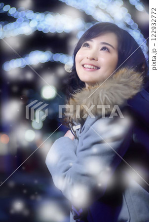 雪の降る中イルミネーションを眺めながら歩く女性 122932772