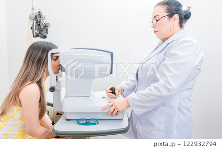 Optometrist checking the eyesight of a patient with an autorefractor. Oculist doing eye exam to female patient Optometrist checking the eyesight of a patient with an autorefractor. Oculist doing eye exam to female patient 122932794