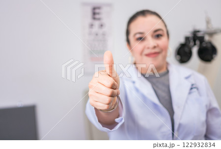 Female optometrist with thumb up in the laboratory. Optometry specialist with thumb up. Smiling eye doctor with thumb up in office Female optometrist with thumb up in the laboratory. Optometry specialist with thumb up. Smiling eye doctor with thumb up in office 122932834