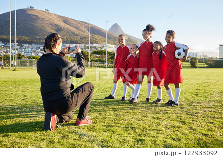 Soccer, phone and team picture with coach, ball and sports girl group with a smile together on a field. Young female football squad happy with post for social media on a sports ground after training 122933092
