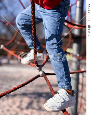 Child climbing rope structure in playground with jeans and sneakers Child climbing rope structure in playground with jeans and sneakers 122933255