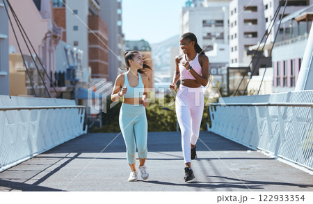 Health women and friends running on bridge in city together for workout and exercise lifestyle. Girl friendship with young, happy and athletic people enjoying cardio fitness run in urban town. Health women and friends running on bridge in city together for workout and exercise lifestyle. Girl friendship with young, happy and athletic people enjoying cardio fitness run in urban town. 122933354