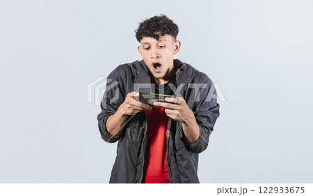 Man amazed holding cell phone horizontally, Guy gasping and playing games on his smartphone Man amazed holding cell phone horizontally, Guy gasping and playing games on his smartphone 122933675