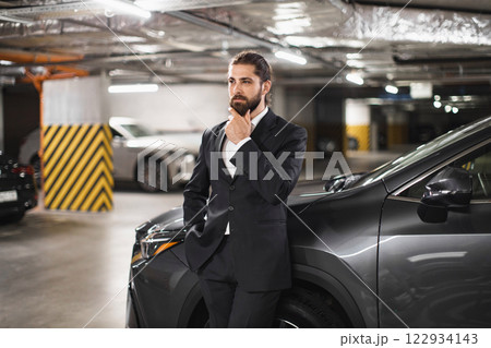 Young Caucasian man in formal suit stands confidently in underground parking lot, reflecting business success and modern lifestyle. Young Caucasian man in formal suit stands confidently in underground parking lot, reflecting business success and modern lifestyle. 122934143