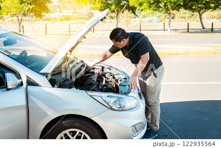Driver checking the oil in his vehicle. Person checking the oil level of his car in the street. Driver inspecting car oil level Driver checking the oil in his vehicle. Person checking the oil level of his car in the street. Driver inspecting car oil level 122935564