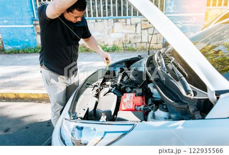 Man checking the oil in his vehicle. Person checking the oil level of his car in the street. Driver inspecting car oil level 122935566