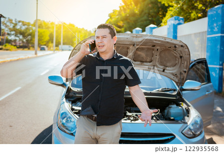 Young man with damaged car calling the mechanic. Driver with the damaged car calling the mechanic. Frustrated man with damaged car calling technician on the road 122935568