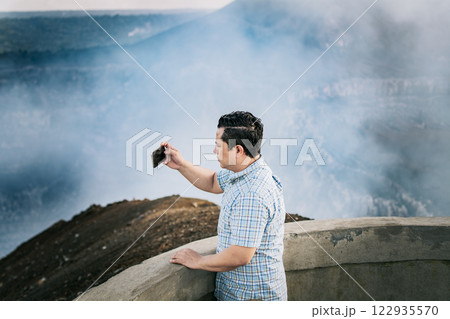 Tourist man taking photos at a viewpoint. Young tourist man taking photos at a volcanic viewpoint. Adventurous man with his cell phone taking photos at a viewpoint 122935570