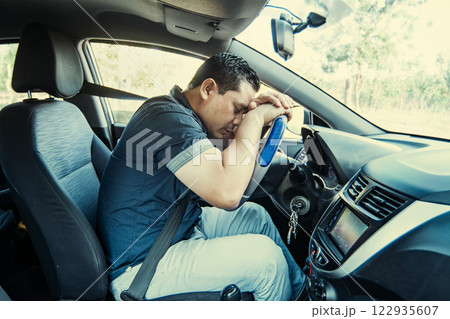 A tired driver asleep at the wheel, concept of man tired of driving. A man driver asleep at the wheel, A tired person sleeping at the wheel of the car 122935607