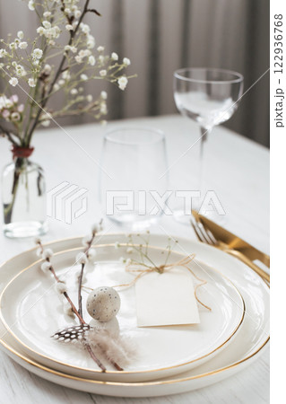 Easter table setting with willow twigs, quail eggs and tag. Golden cutlery and golden rim plates. 122936768