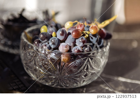 Close-up of blue fresh juicy grapes in a crystal vase. Fragrant berries in a glass plate on a marble black table. 122937513