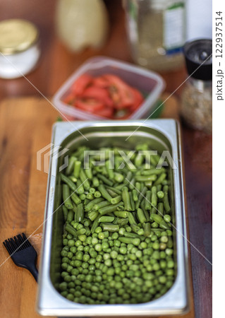 Cooking a healthy vegetarian dish. A metal bowl with fresh green peas on a wooden table. Ingredients for a delicious lunch. 122937514