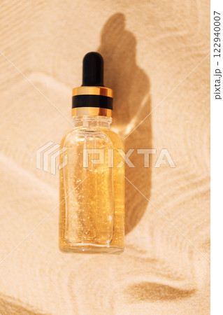A mock-up glass bottle with a pipette with an intensive moisturizing concentrate with hyaluronic acid and vitamins on a background of sand. 122940007