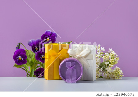 A spring greeting composition of purple viola flowers and cherry blossom branches with yellow, white and purple gift boxes on gray table. Concept of spring, Easter, Mother's Day, happy Valentine's Day 122940575
