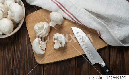 Fresh champignon mushrooms. Cutting champignon on cutting board. 122940595