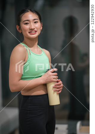 室内のジムでトレーニングの合間に水分補給をする若い女性 122942930