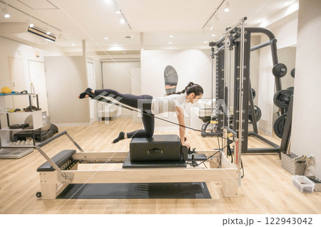 室内のジムでマシンピラティスをする若い女性 122943042