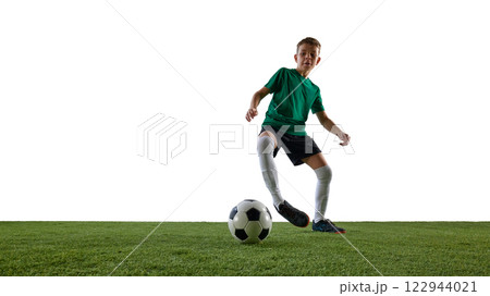Dynamic image of focused boy, soccer player in green jersey and black short in motion, dribbling ball against white studio background Dynamic image of focused boy, soccer player in green jersey and black short in motion, dribbling ball against white studio background 122944021