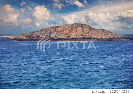 Island on the horizon. Rocks in the sea. Beautiful rocky seascape with cloudy sky. View from ship Island on the horizon. Rocks in the sea. Beautiful rocky seascape with cloudy sky. View from ship 122944232