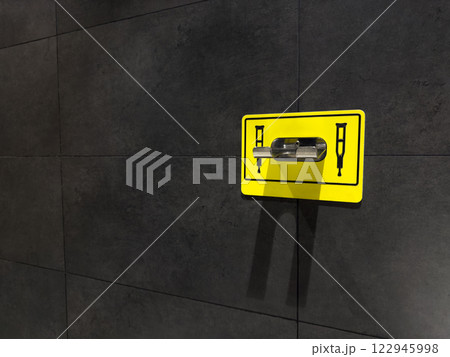 Sign with symbol of crutches and clamp on wall for attaching crutches in toilet. Convenient device for creating comfortable living conditions for people with disabilities. Device for hang crutches Sign with symbol of crutches and clamp on wall for attaching crutches in toilet. Convenient device for creating comfortable living conditions for people with disabilities. Device for hang crutches 122945998
