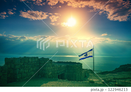Beautiful sunrise over Masada fortress. Ruins of King Herod's palace in the Judaean Desert. The flag of Israel fluttering on Masada Beautiful sunrise over Masada fortress. Ruins of King Herod's palace in the Judaean Desert. The flag of Israel fluttering on Masada 122946213