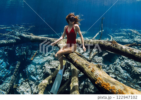 Woman freediver sitting underwater on sunken log in crystal blue water. Freediving in fresh water lake in Indonesia 122947102