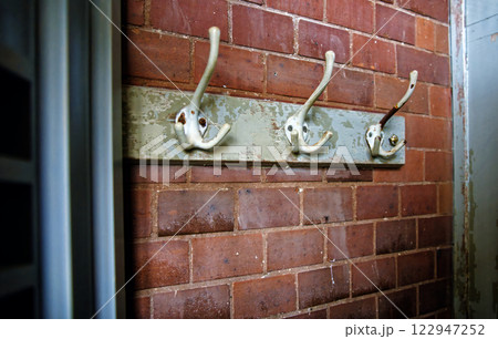 Old coat hooks on wooden board against brick wall 122947252