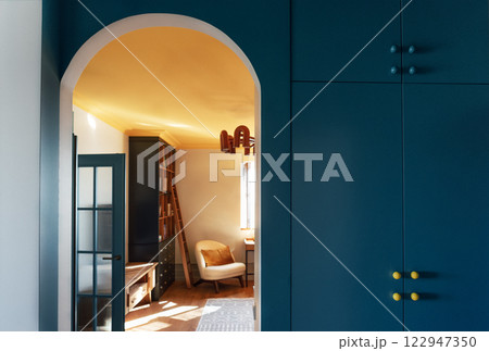 Cozy stylish interior of the living room. An arched doorway with a bright blue wall and a built-in wardrobe. Contrasting design with natural wooden furniture. 122947350