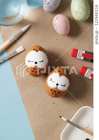 Easter eggs with sleeping owls, hand-painted with acrylics, on a background of paints, brushes and palettes. DIY concept Easter eggs with sleeping owls, hand-painted with acrylics, on a background of paints, brushes and palettes. DIY concept 122948116