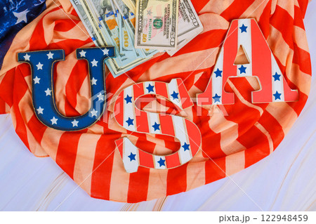 USA letters sit top striped fabric with dollar bills, symbolizing patriotism finance celebration. 122948459