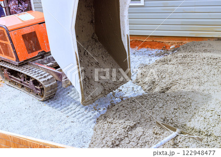 Wheelbarrow tracked machine pours fresh concrete onto prepared surface for new residential foundation under construction. 122948477