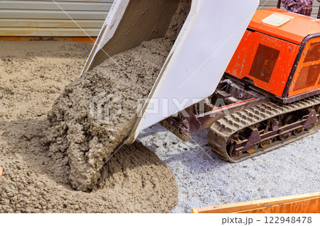 Construction workers use rubber wheelbarrow machinery to pour concrete on building site, preparing for foundation slab 122948478